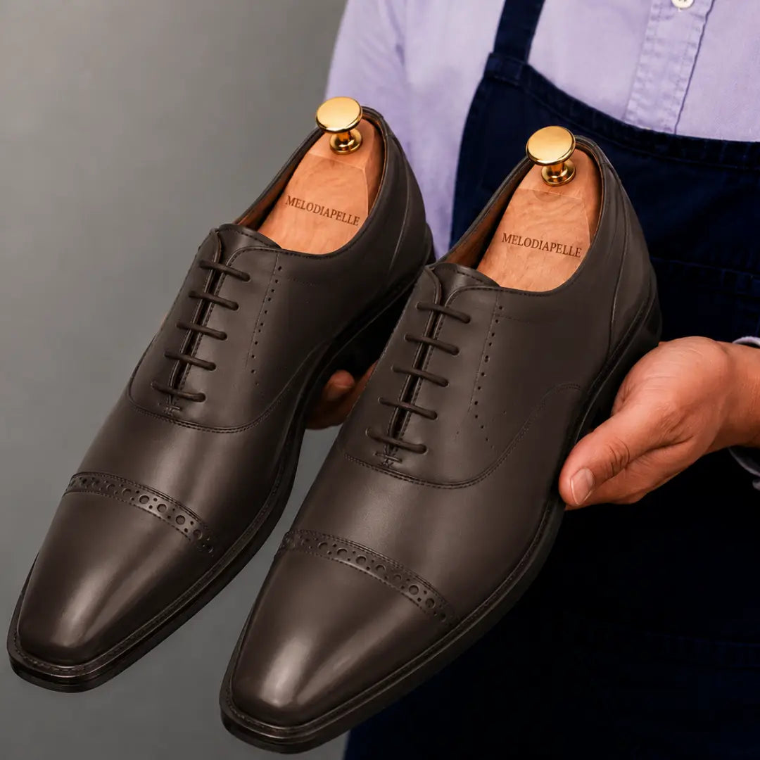 Man holding a pair of Melodiapelle Marcello Semi-Brogue Oxford shoes in brown leather, close-up