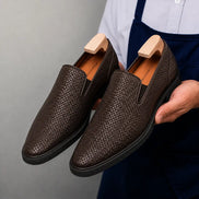 Man holding a pair of Melodiapelle Marengo Embossed Slip-On Sneakers in brown leather, close-up