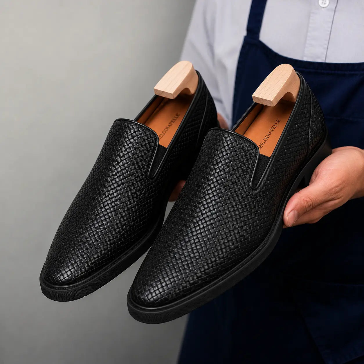 Man holding a pair of Melodiapelle Marengo Embossed Slip-On Sneakers in nero black leather, close-up