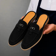 Man holding a pair of Melodiapelle Maria Mule shoes in black suede, close-up