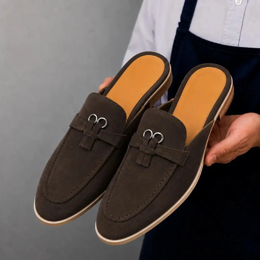 Man holding a pair of Melodiapelle Maria Mule shoes in dark brown suede, close-up