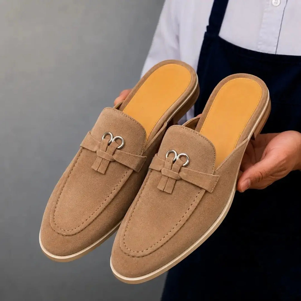 Man holding a pair of Melodiapelle Maria Mule shoes in sand beige suede, close-up