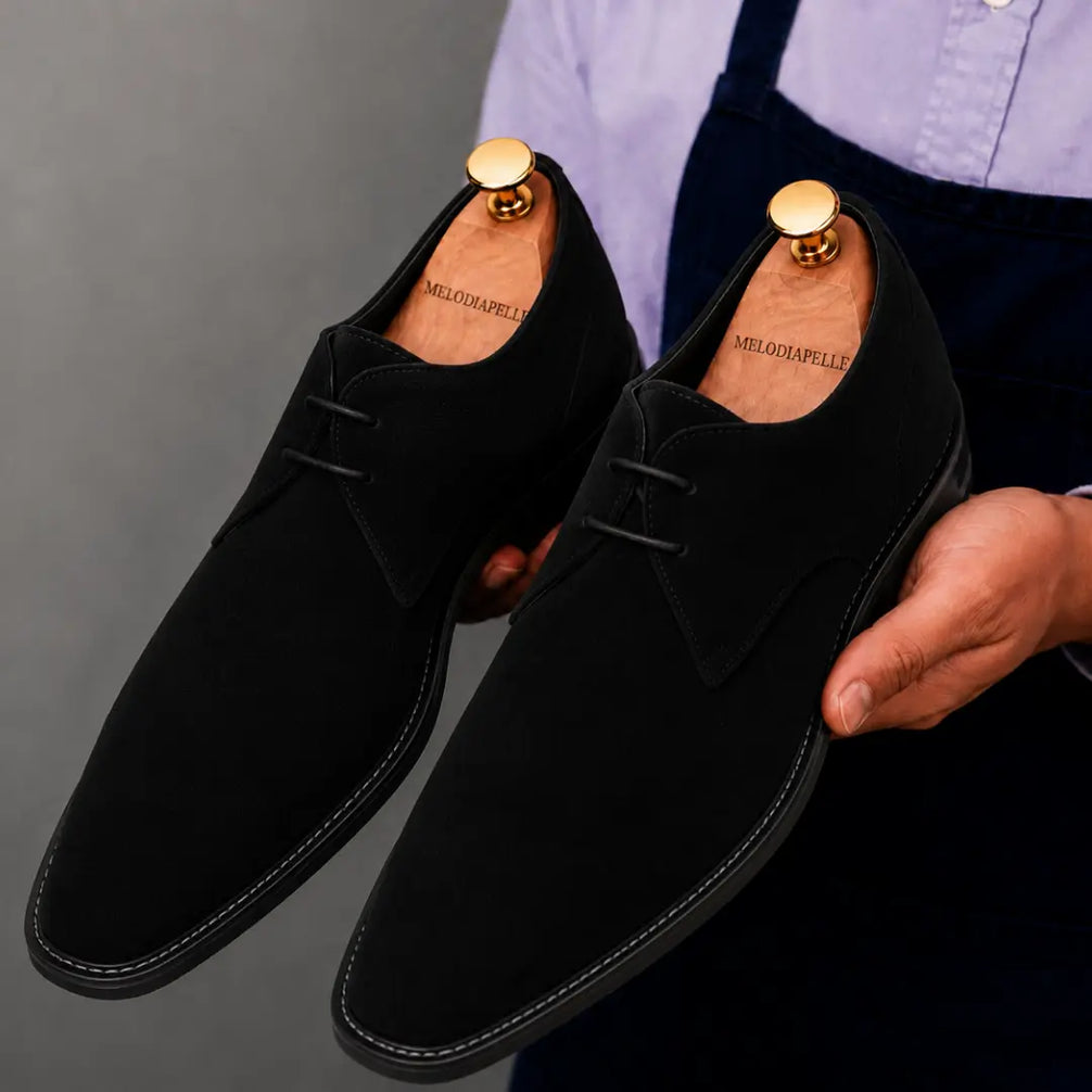 Man holding a pair of Melodiapelle Maringa Suede Chukka Boots in black suede, close-up