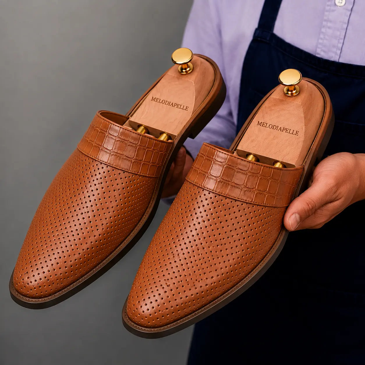 Man holding a pair of Melodiapelle Marshall Mules in tan leather, close-up