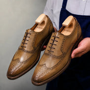 Man holding a pair of Melodiapelle Marshfield Wingtip Brogue Oxford shoes in olive khaki leather, close-up