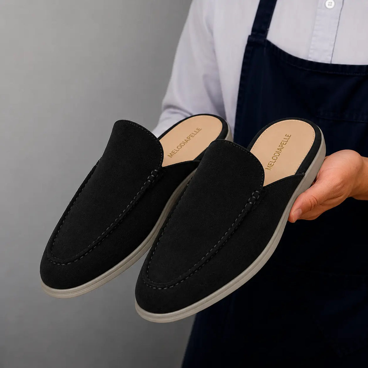 Man holding a pair of Melodiapelle Martia Mule shoes in black suede, close-up