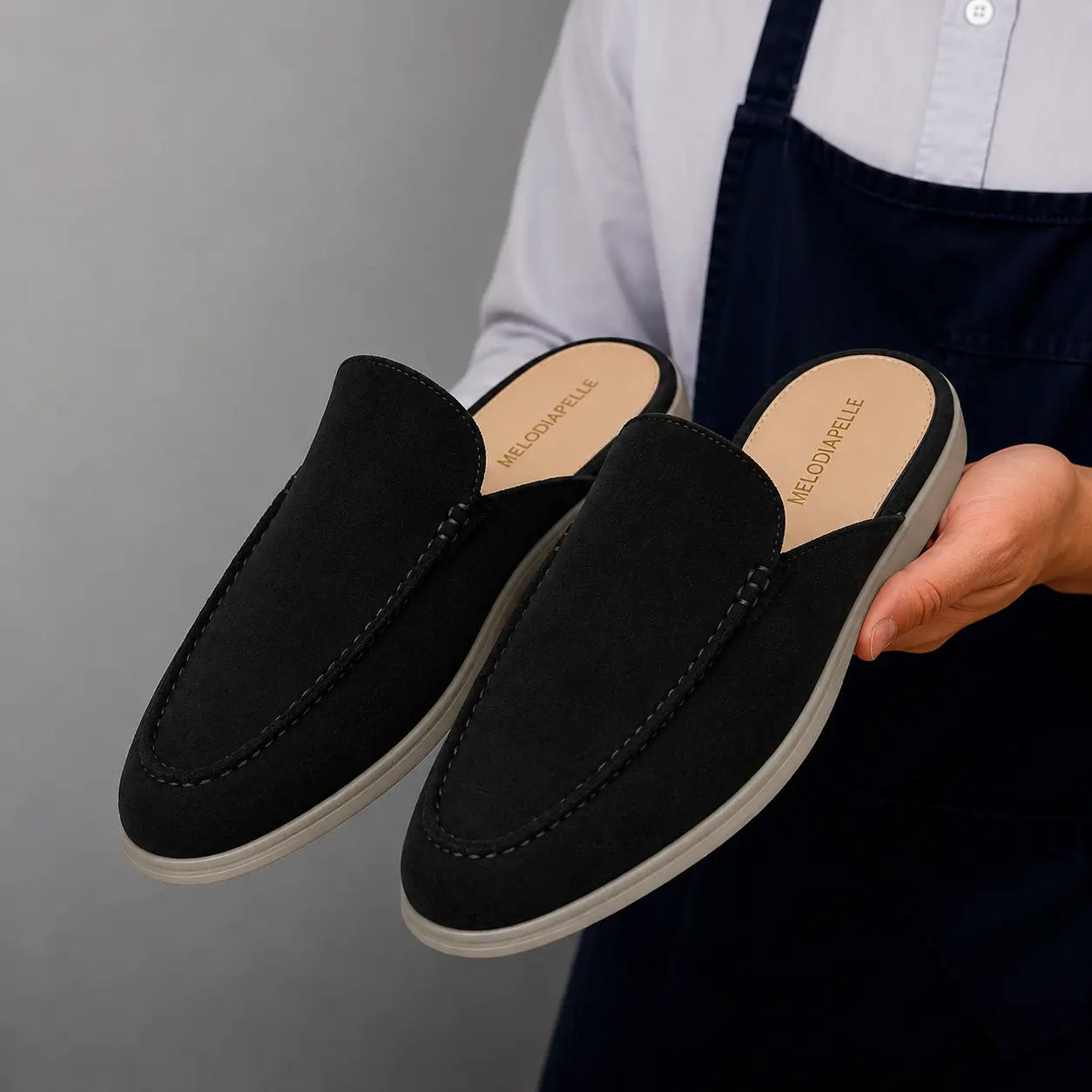 Man holding a pair of Melodiapelle Martia Mule shoes in black suede, close-up