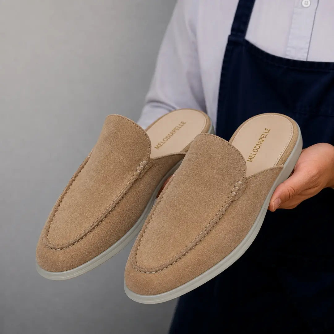 Man holding a pair of Melodiapelle Martia Mule shoes in sand beige suede, close-up