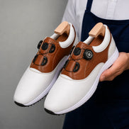 Man holding a pair of Melodiapelle Marzano BOA Golf Shoes in white and tan leather, close-up