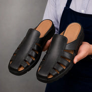 Man holding a pair of Melodiapelle Mason Mules in black leather, close-up