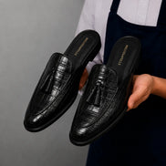Man holding a pair of Melodiapelle Mason Mule shoes in black croc-embossed leather, close-up