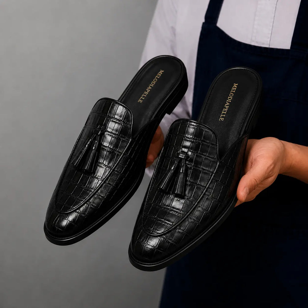 Man holding a pair of Melodiapelle Mason Mule shoes in black croc-embossed leather, close-up