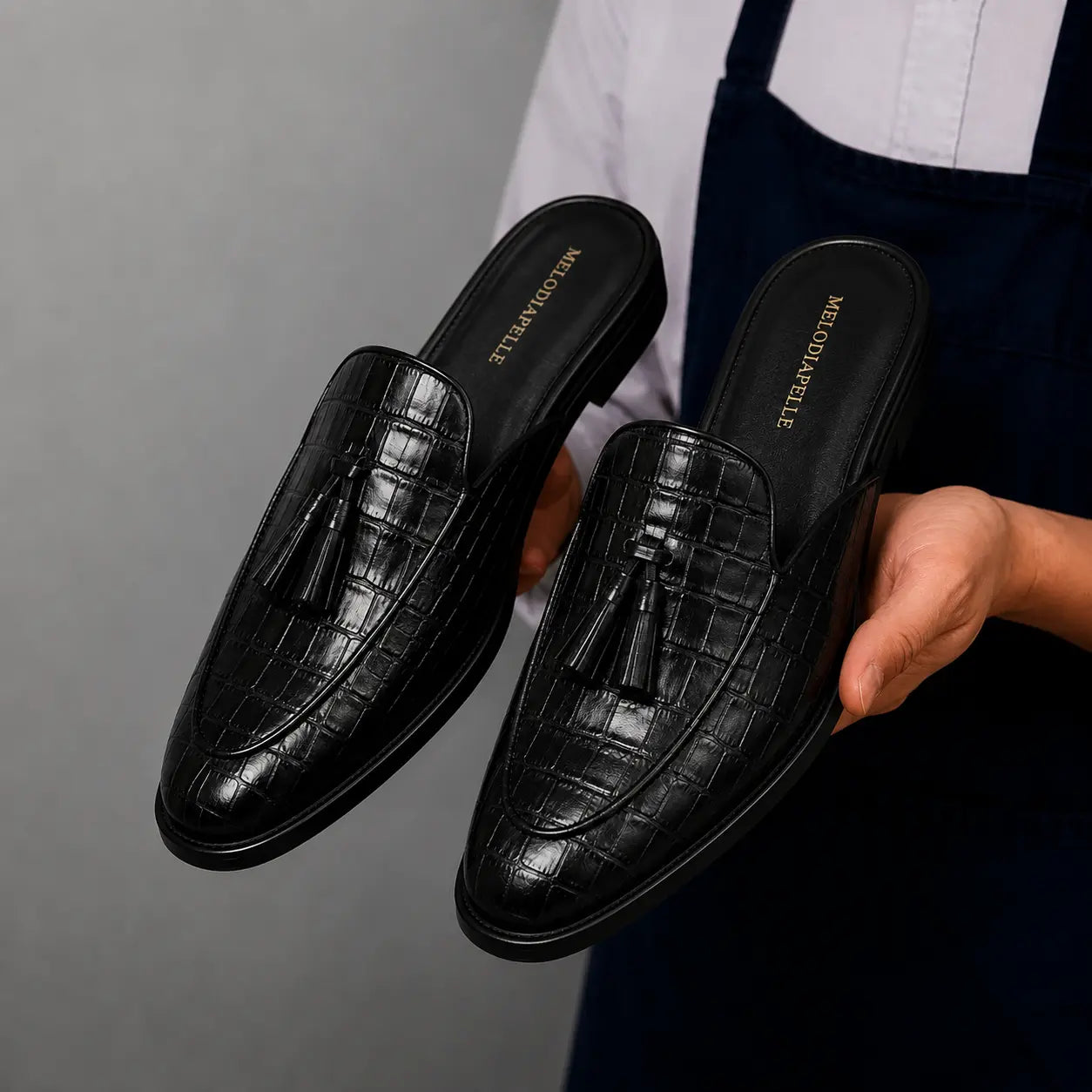Man holding a pair of Melodiapelle Mason Mule shoes in black croc-embossed leather, close-up