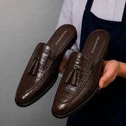 Man holding a pair of Melodiapelle Mason Mule shoes in dark brown croc-embossed leather, close-up