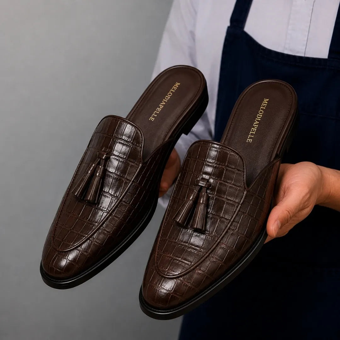 Man holding a pair of Melodiapelle Mason Mule shoes in dark brown croc-embossed leather, close-up