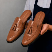 Man holding a pair of Melodiapelle Mason Mule shoes in tan croc-embossed leather, close-up
