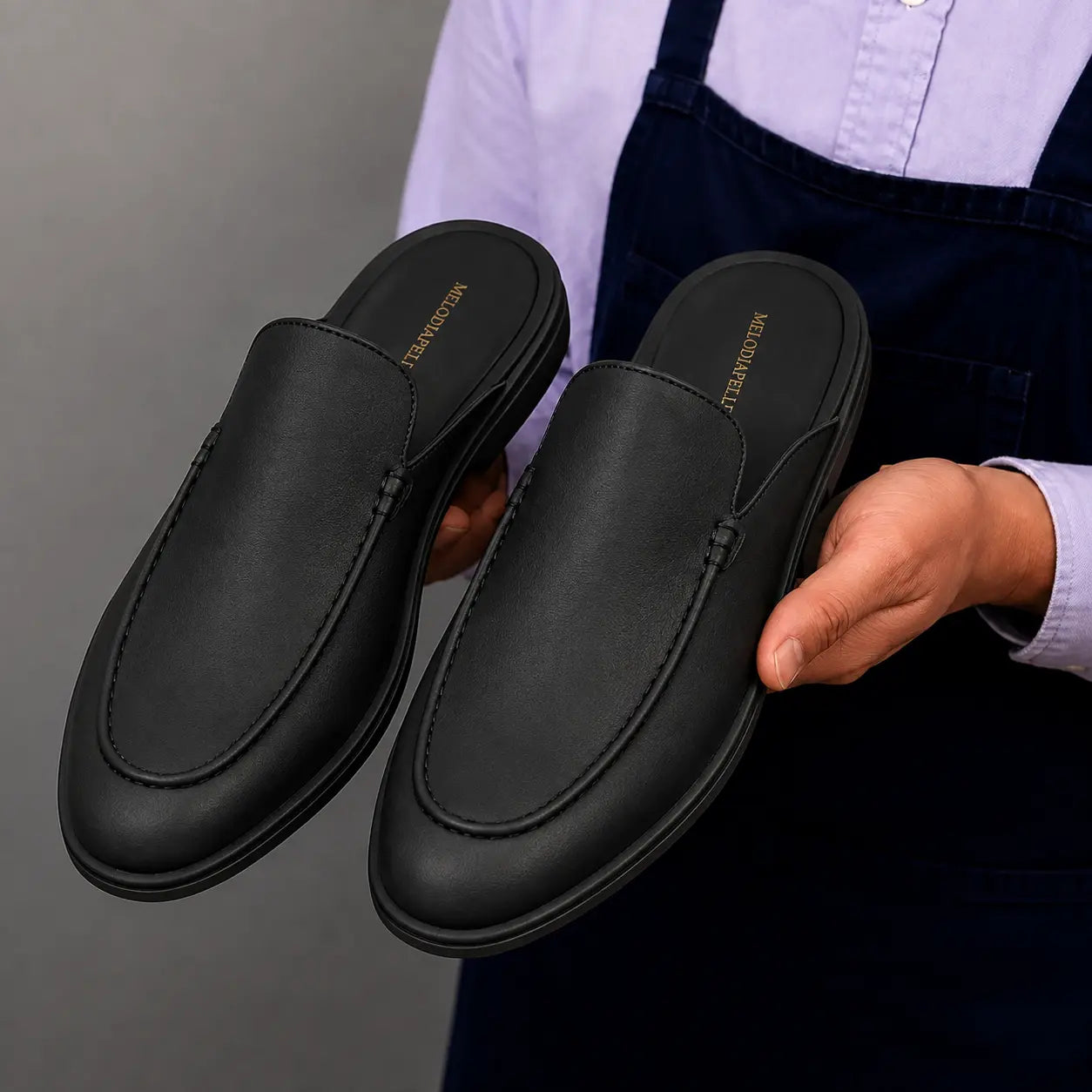 Man holding a pair of Melodiapelle Massimo Mule shoes in black leather, close-up