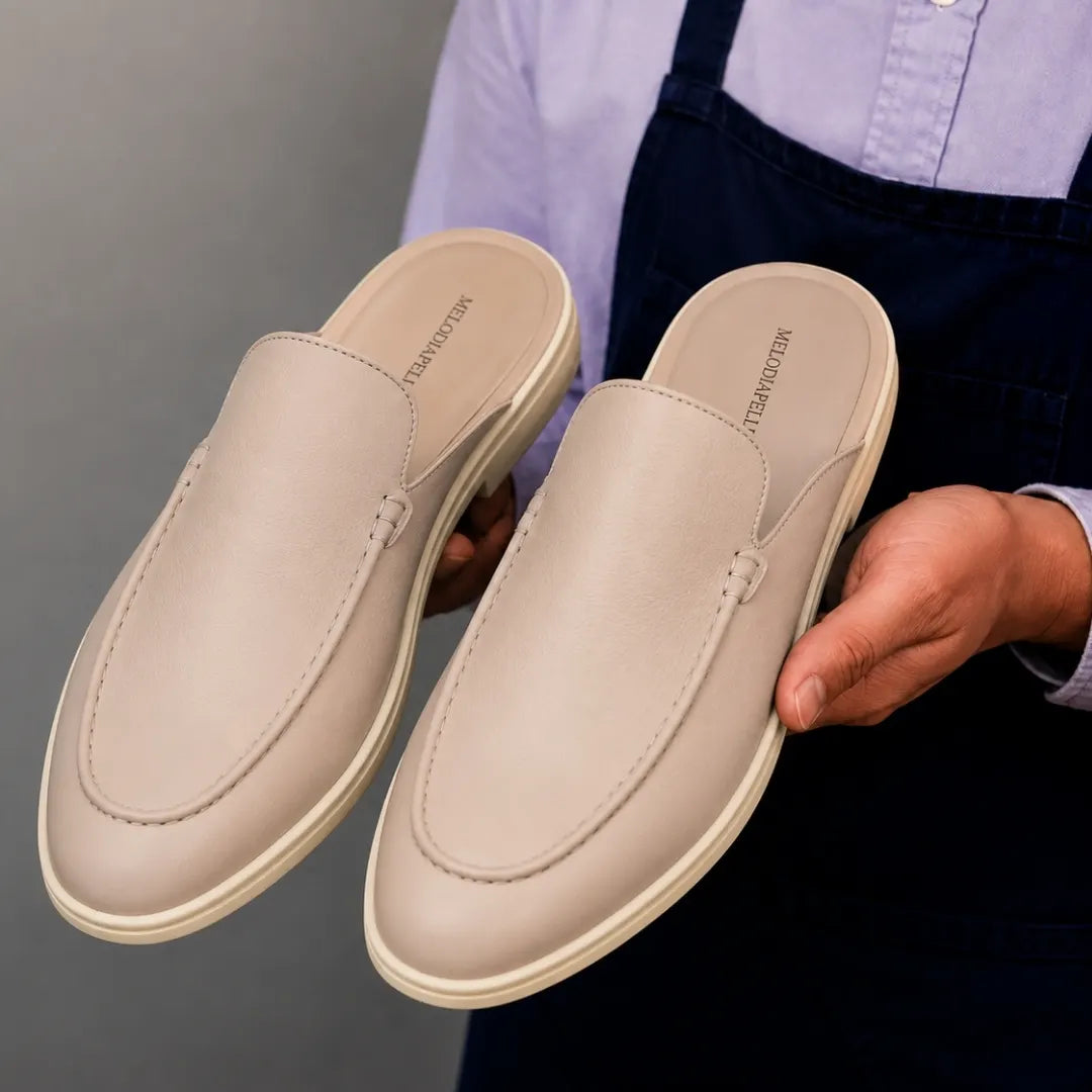 Man holding a pair of Melodiapelle Massimo Mule shoes in cream beige leather, close-up
