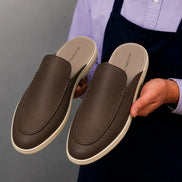 Man holding a pair of Melodiapelle Massimo Mule shoes in dark brown leather, close-up