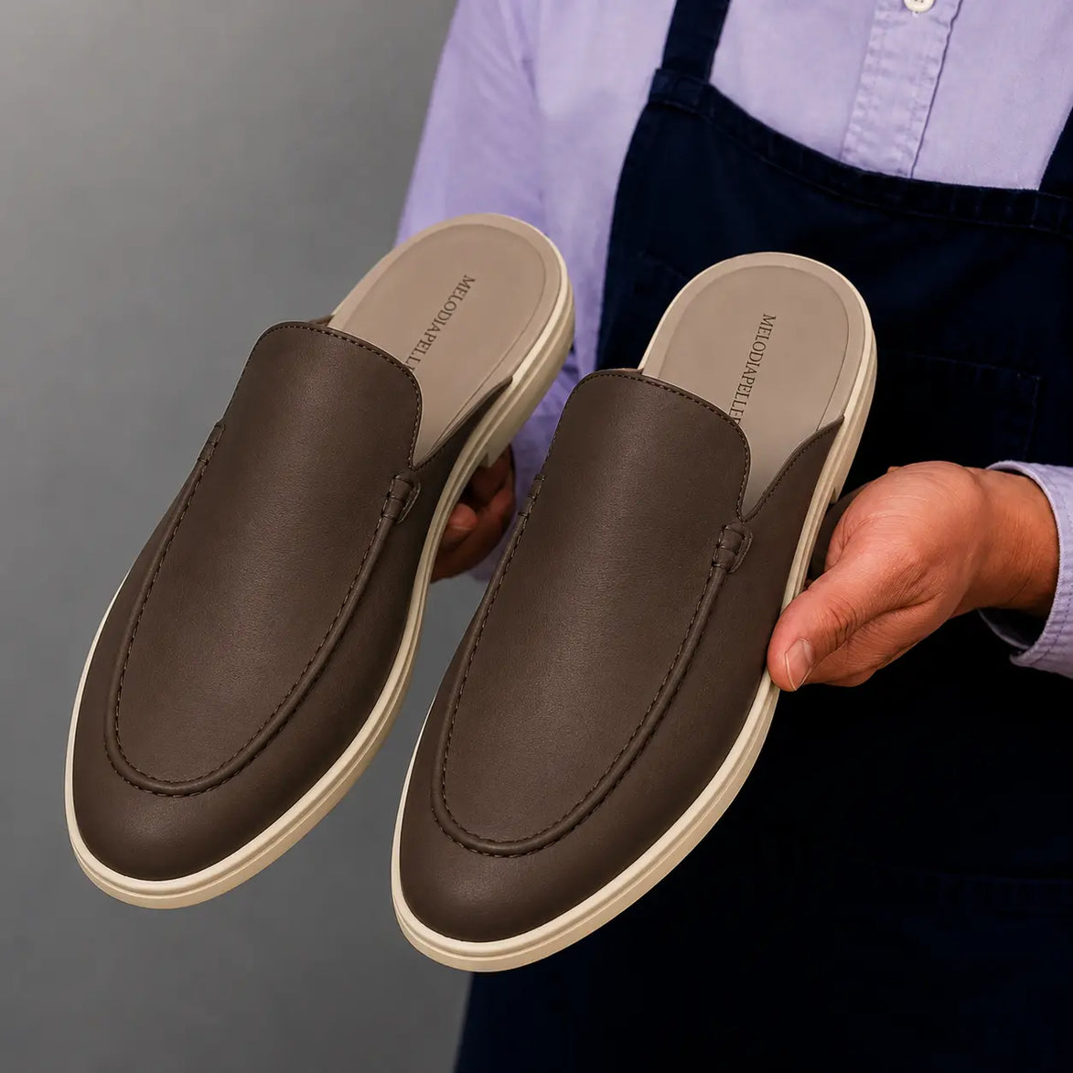 Man holding a pair of Melodiapelle Massimo Mule shoes in dark brown leather, close-up