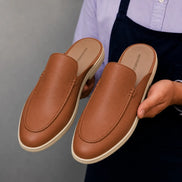 Man holding a pair of Melodiapelle Massimo Mule shoes in tan leather, close-up