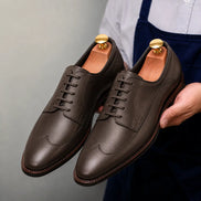 Man holding a pair of Melodiapelle Matador Apron-Toe Derby shoes in dark brown leather, close-up