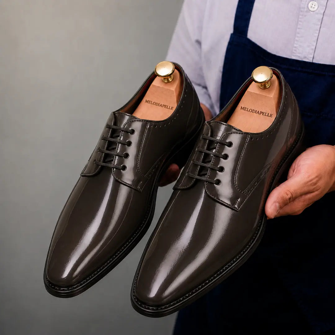 Man holding a pair of Melodiapelle Matera Plain-Toe Derby shoes in brown leather, close-up