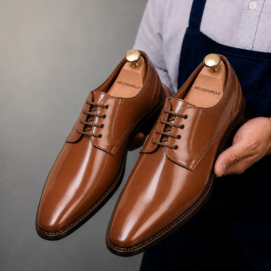 Man holding a pair of Melodiapelle Matera Plain-Toe Derby shoes in tan leather, close-up
