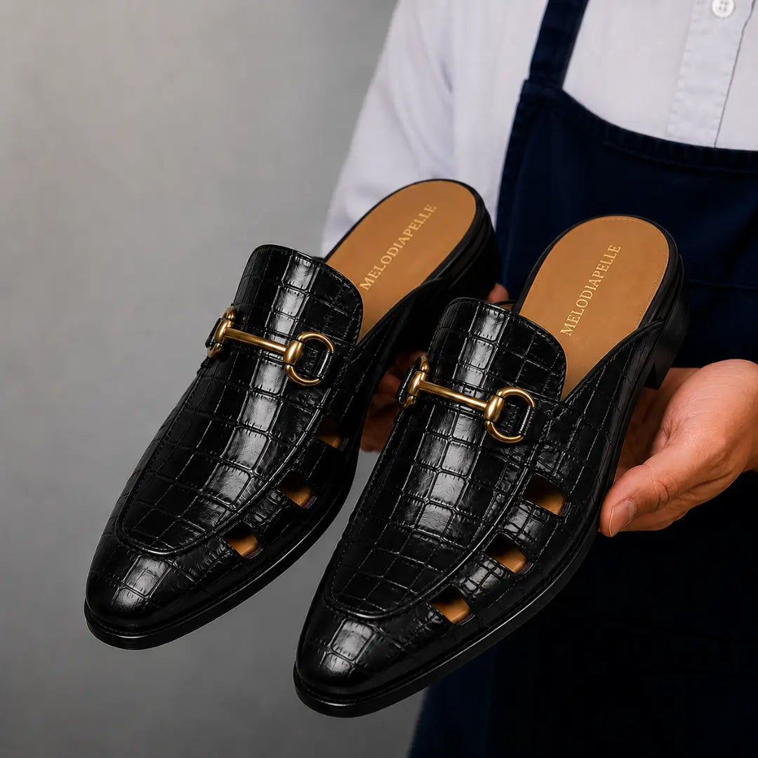 Man holding a pair of Melodiapelle Matilda Mule shoes in black croc-embossed leather, close-up