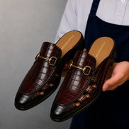 Man holding a pair of Melodiapelle Matilda Mule shoes in oxblood brown croc-embossed leather, close-up