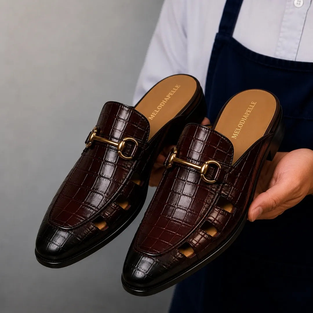 Man holding a pair of Melodiapelle Matilda Mule shoes in oxblood brown croc-embossed leather, close-up