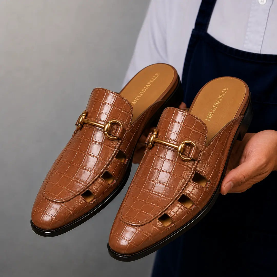 Man holding a pair of Melodiapelle Matilda Mule shoes in tan croc-embossed leather, close-up