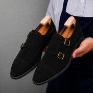 Man holding a pair of Melodiapelle Maverick Double Monk Brogue shoes in black suede, close-up