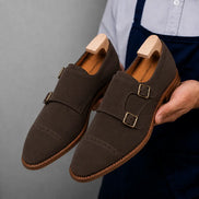 Man holding a pair of Melodiapelle Maverick Double Monk Brogue shoes in dark brown suede, close-up