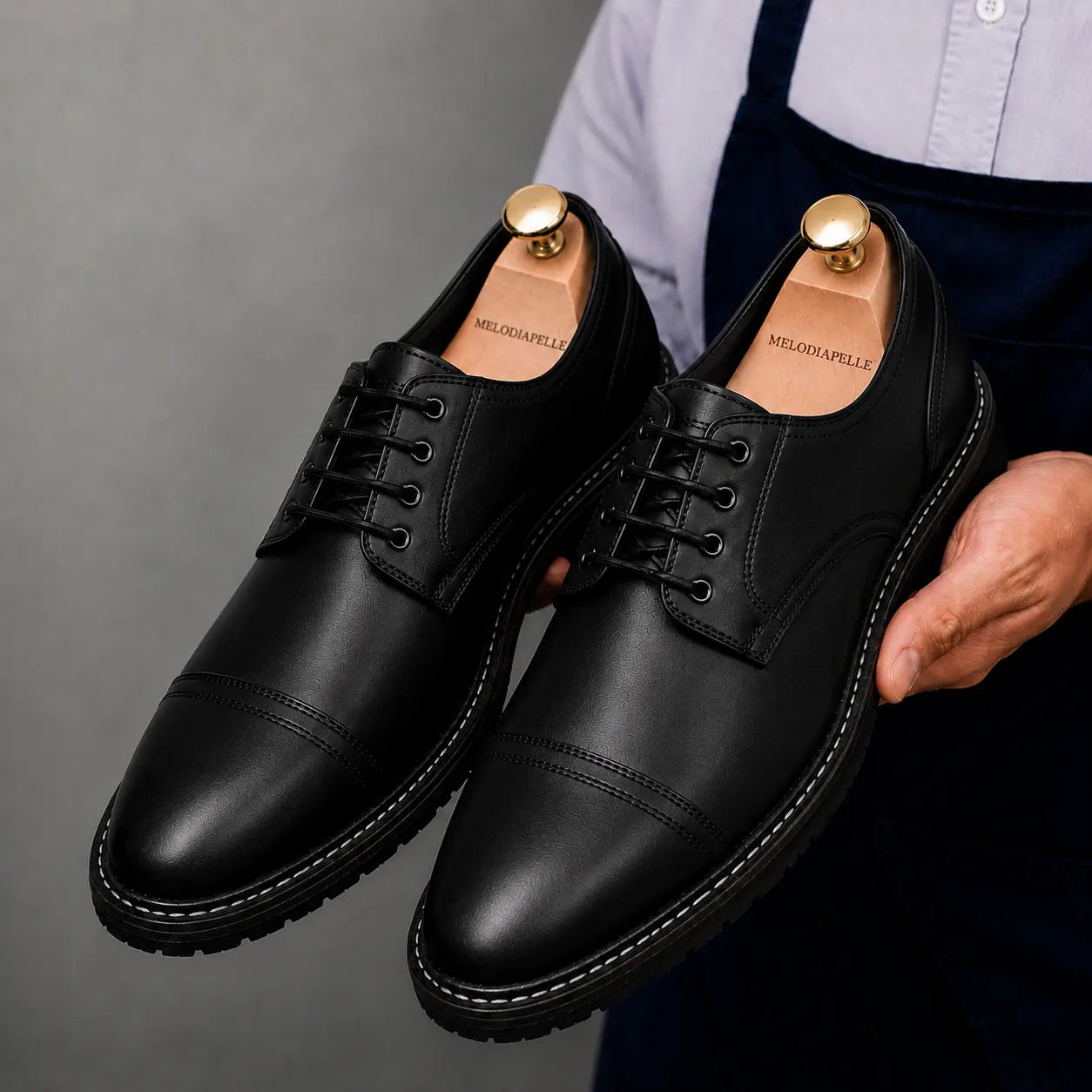 Man holding a pair of Melodiapelle Max Cap Toe Derby shoes in black leather, close-up