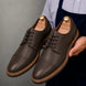 Man holding a pair of Melodiapelle Max Cap Toe Derby shoes in dark brown leather, close-up