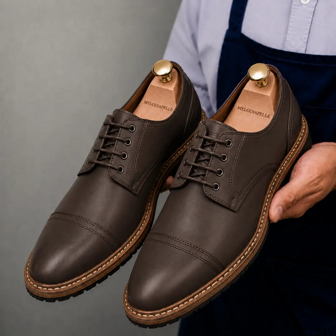 Man holding a pair of Melodiapelle Max Cap Toe Derby shoes in dark brown leather, close-up