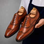 Man holding a pair of Melodiapelle Mazaro Wingtip Brogue Oxford shoes in cognac tan leather, close-up