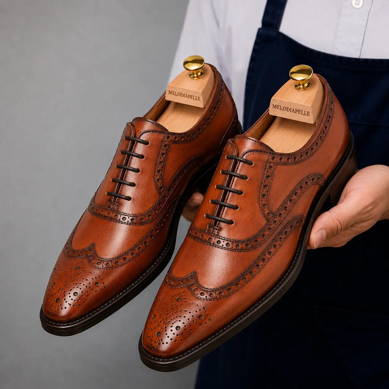 Man holding a pair of Melodiapelle Mazaro Wingtip Brogue Oxford shoes in cognac tan leather, close-up