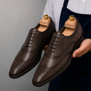 Man holding a pair of Melodiapelle Mazaro Wingtip Brogue Oxford shoes in dark brown leather, close-up