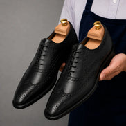 Man holding a pair of Melodiapelle Mazaro Wingtip Brogue Oxford shoes in nero black leather, close-up