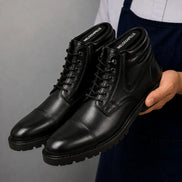 Man holding a pair of Melodiapelle Mcallen Combat Boots in black leather, close-up