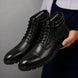 Man holding a pair of Melodiapelle Mcallen Combat Boots in black leather, close-up