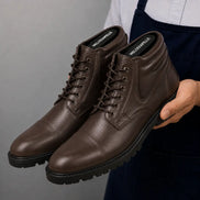 Man holding a pair of Melodiapelle Mcallen Combat Boots in dark brown leather, close-up