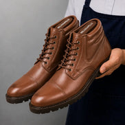 Man holding a pair of Melodiapelle Mcallen Combat Boots in tan leather, close-up