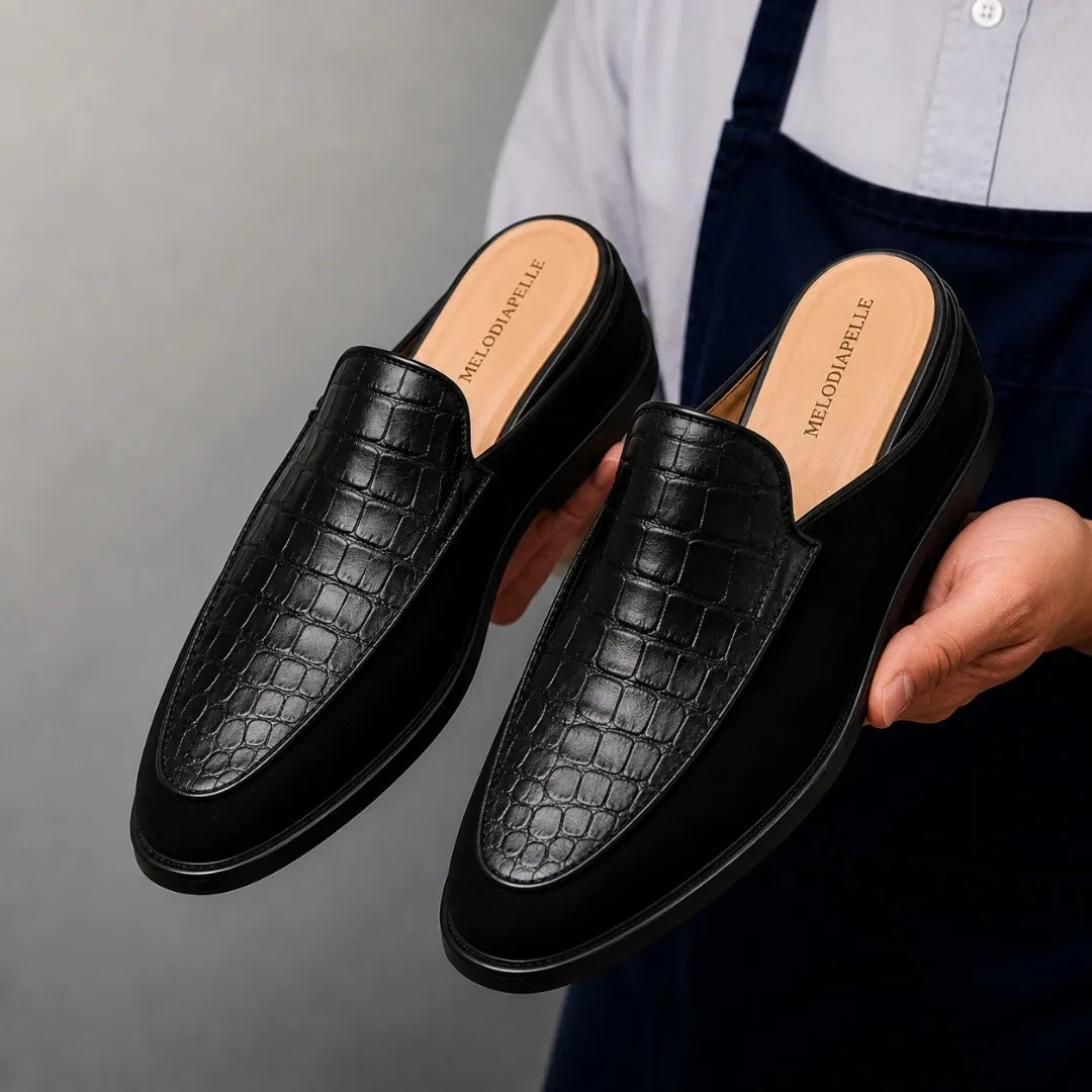 Man holding a pair of Melodiapelle Mckinsey Mule shoes in black croc-embossed leather, close-up