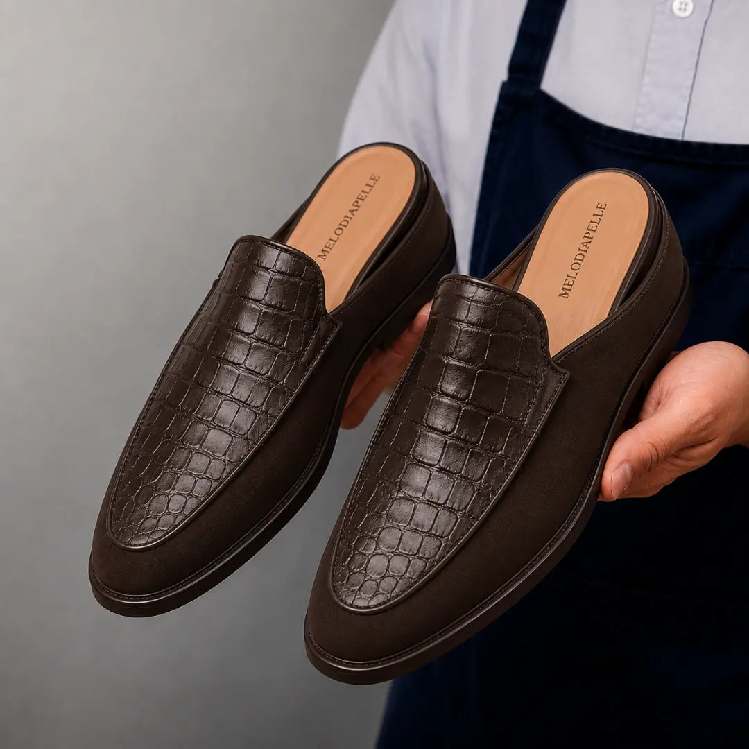 Man holding a pair of Melodiapelle Mckinsey Mule shoes in dark brown croc-embossed leather, close-up