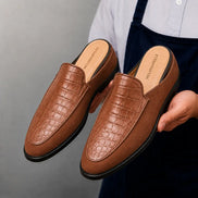 Man holding a pair of Melodiapelle Mckinsey Mule shoes in tan croc-embossed leather, close-up