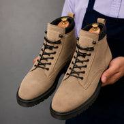 Man holding a pair of Melodiapelle Meilbourne Combat Boots in sand beige suede, close-up