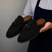 Man holding a pair of Melodiapelle Mendiai Mule shoes in black suede, close-up